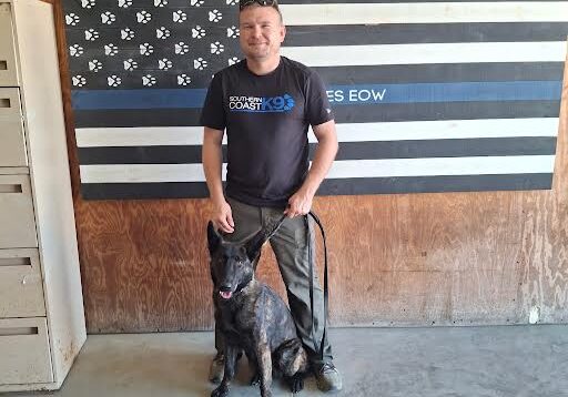 Man with dog in front of flag.