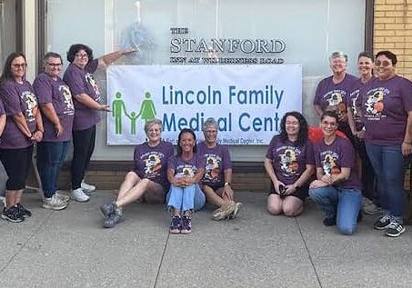 Group in purple shirts by medical center sign.