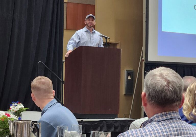 Man speaking at a conference podium, audience listening.