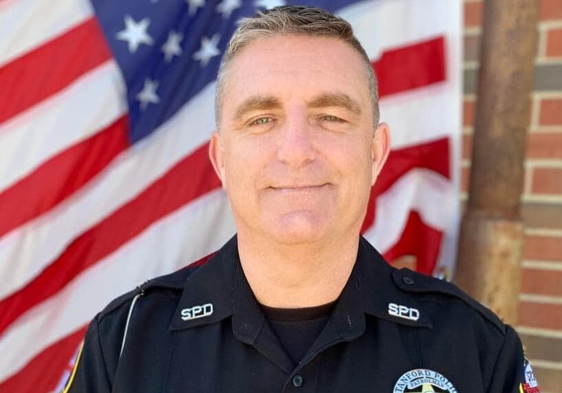 Police officer standing in front of American flag.