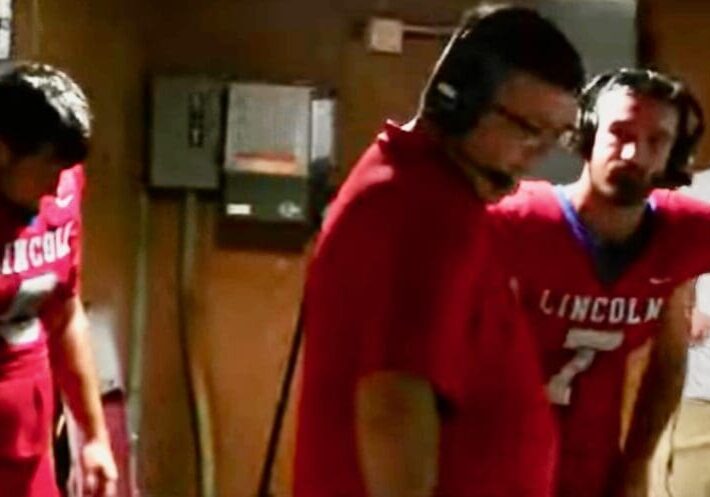 Football players and coaches wearing headsets indoors.