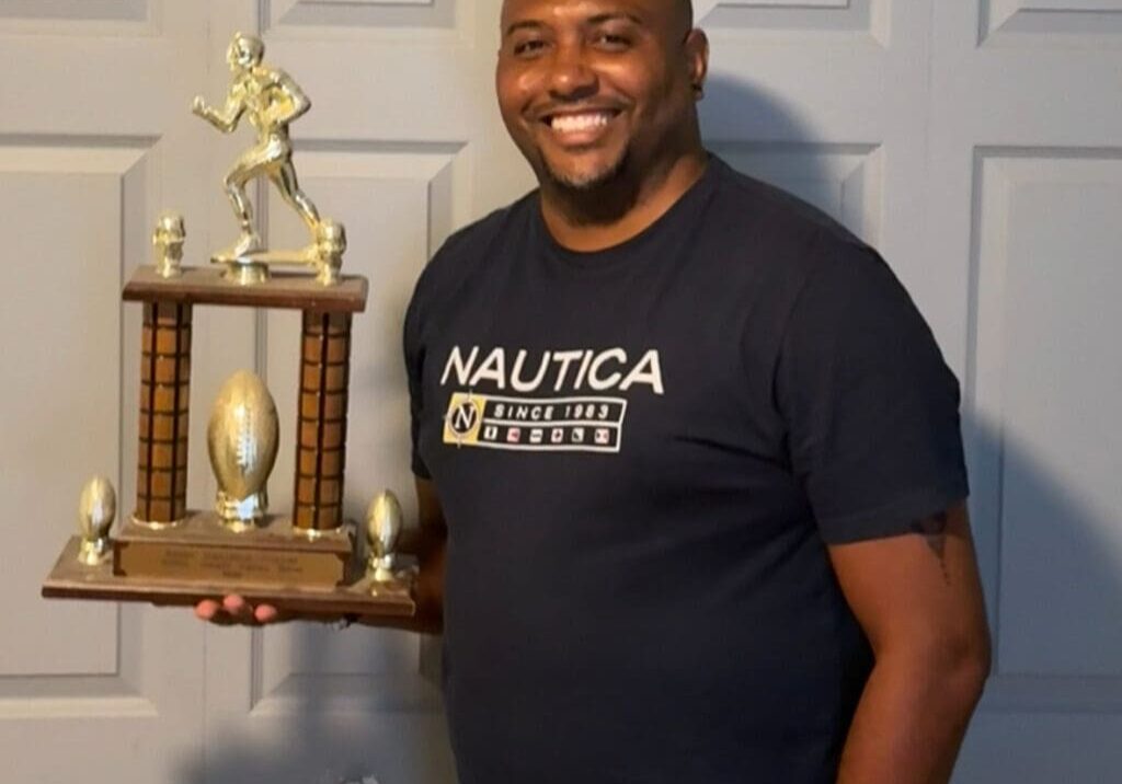 Man holding a football trophy, smiling.