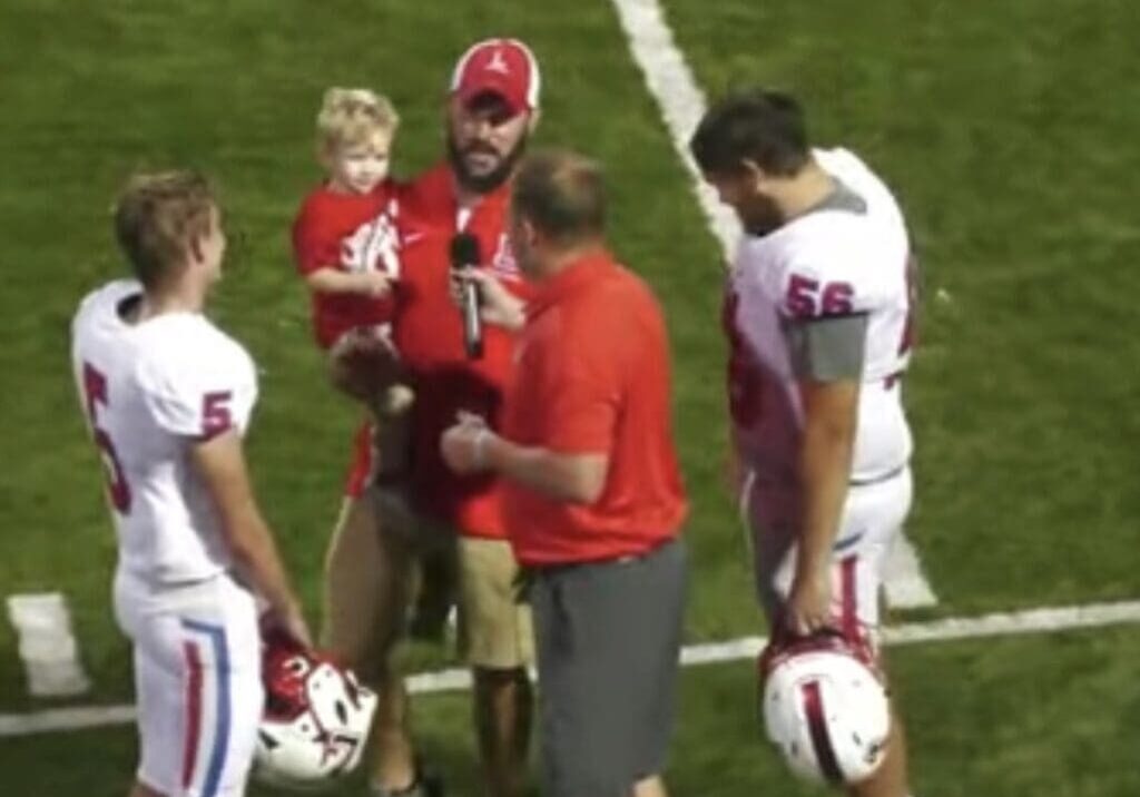 Football players and coach with child on field.