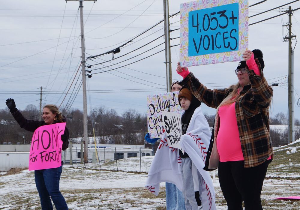 People holding protest signs on snowy roadside.