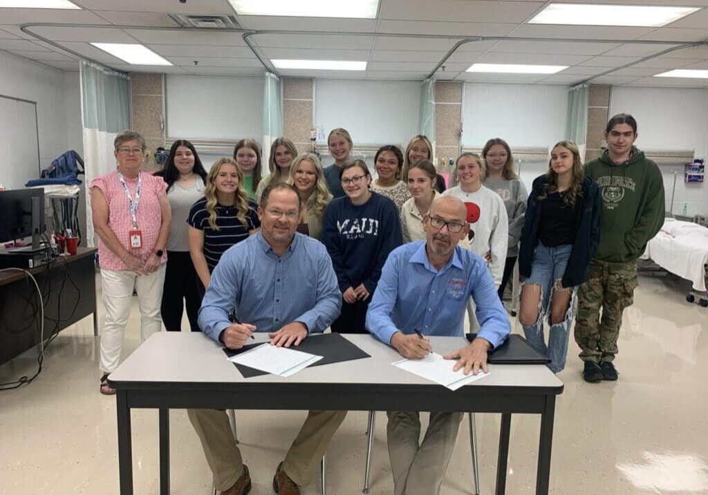 People signing documents with group behind.