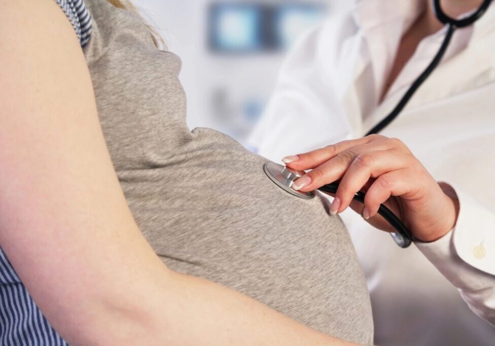 Doctor examining pregnant woman's belly with stethoscope.